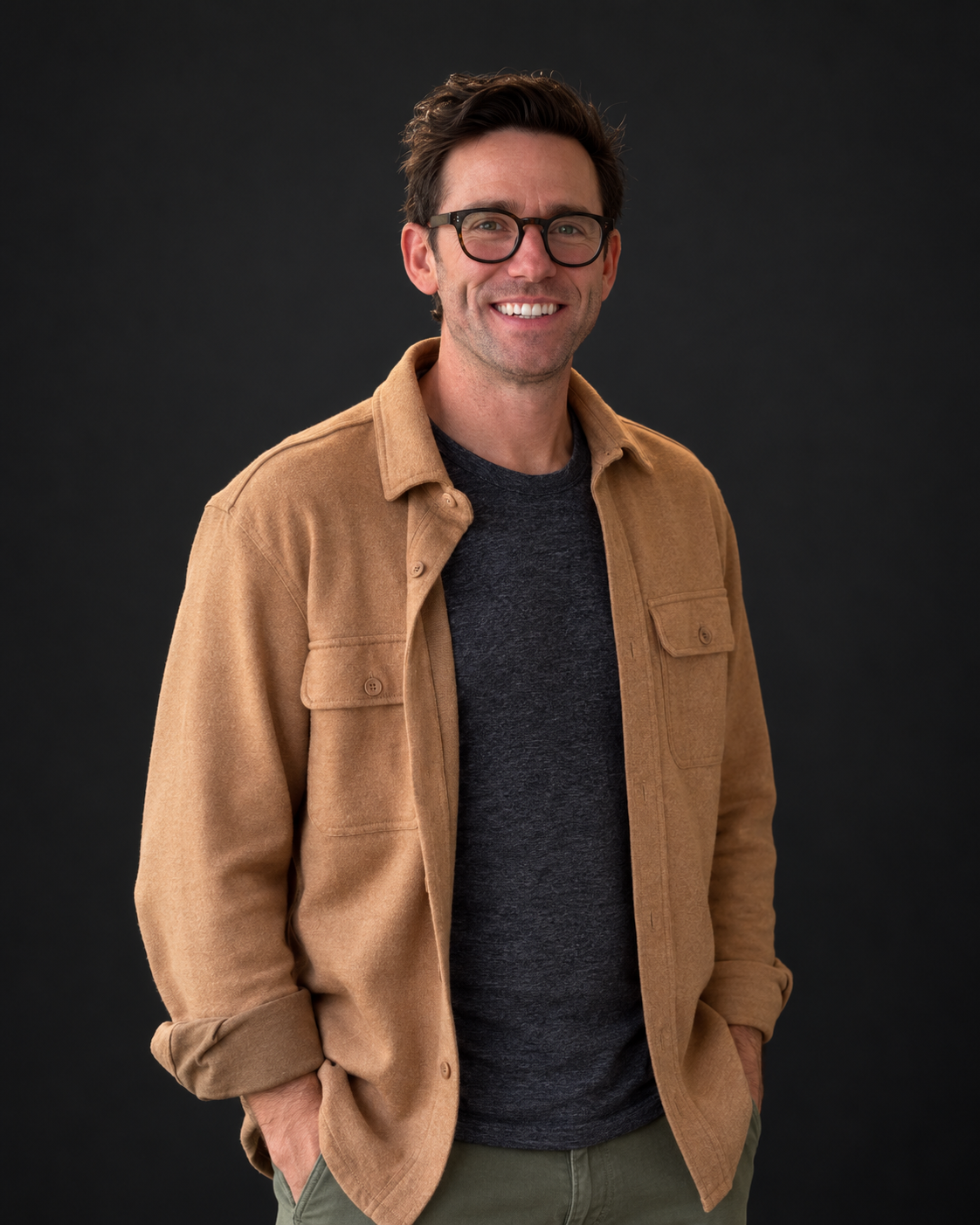 Kevin R. Kelly in glasses and a tan jacket, photographed with natural studio-style lighting